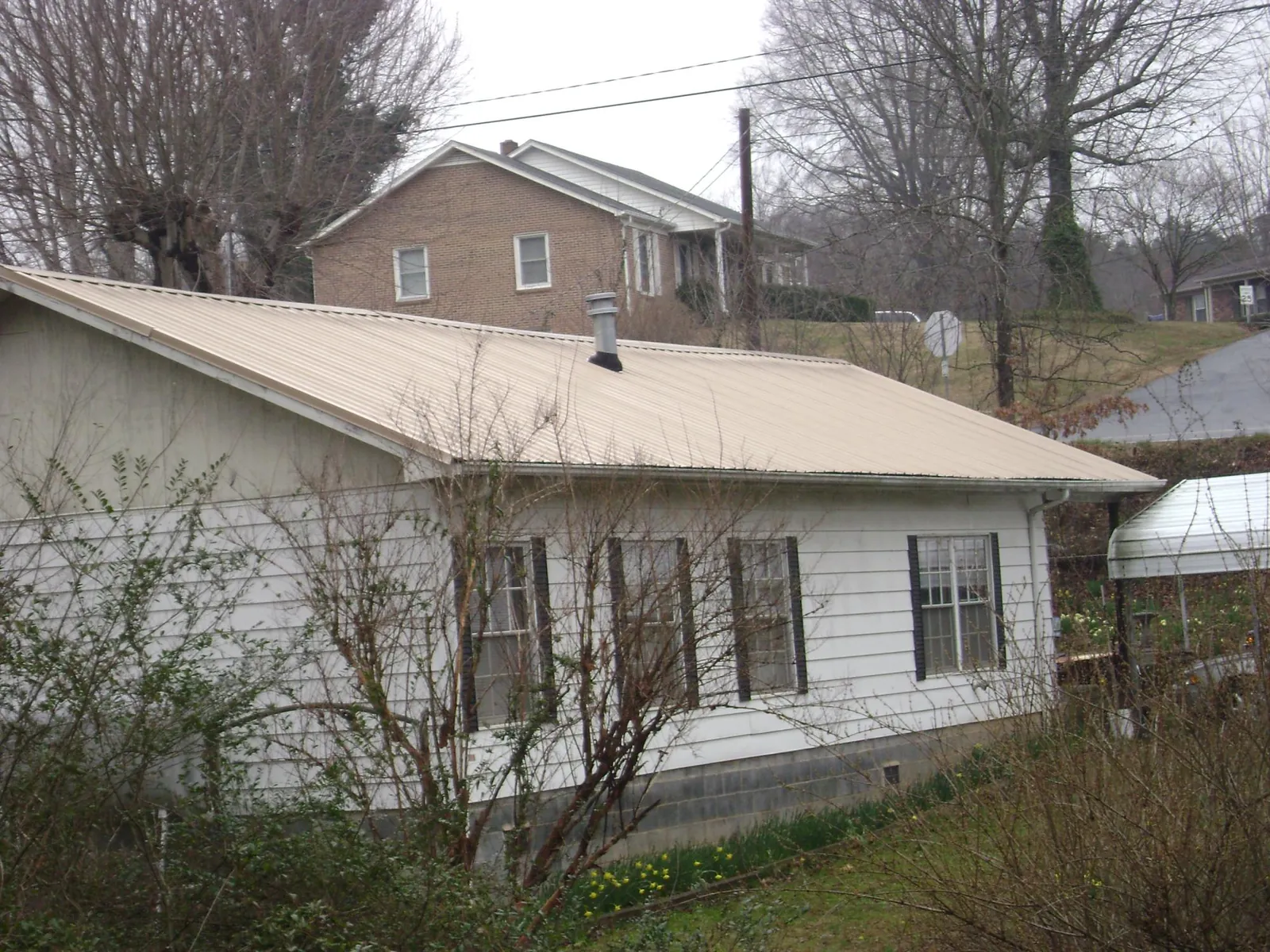 Tan metal roof on a white sided house set into a hillside — Commercial Roofing by Roofing Brothers in Westfield