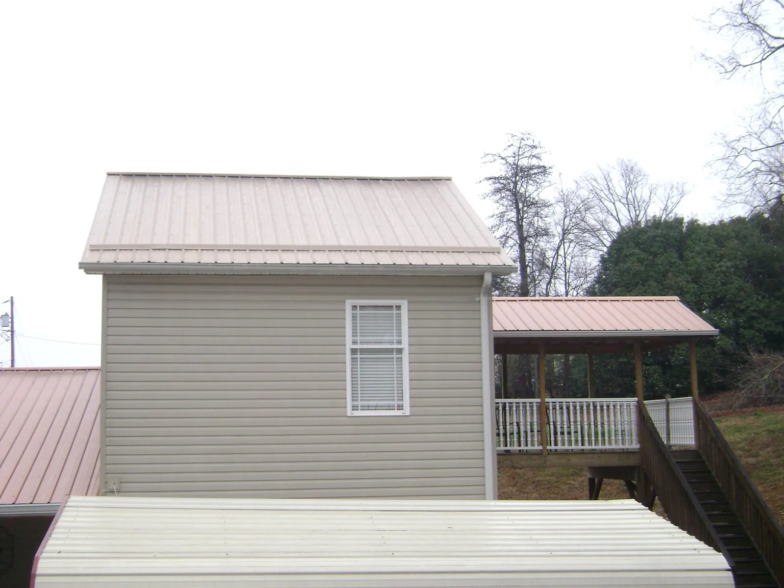 Tan metal roofs on a two story addition and attached porch, from a Roof Replacement job in Westfield